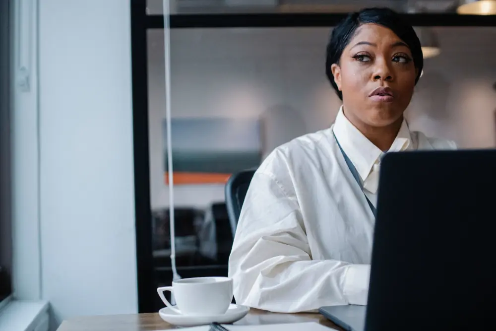 A manager looking up from her laptop in a glass walled office