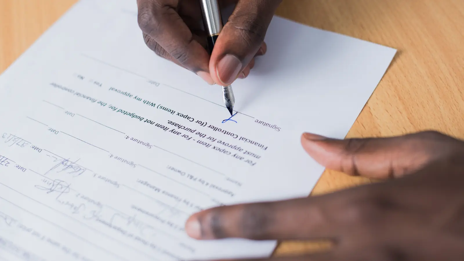 A hand signing the approval line of a financial request form